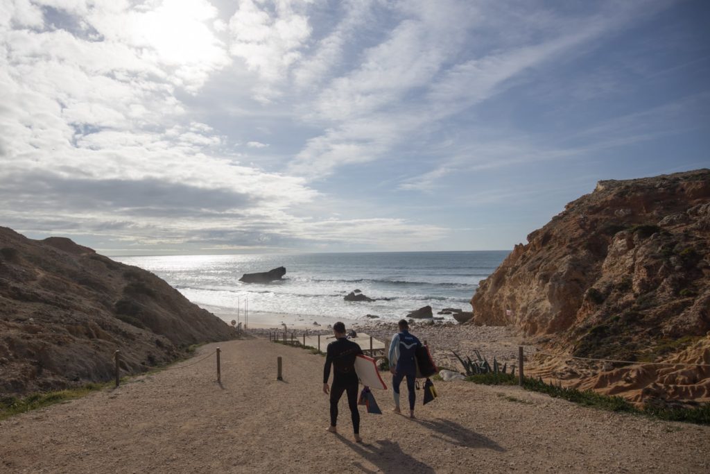 Two bodyboarders carrying their boards walking towards Tonel Beach in Sagres, Portugal.