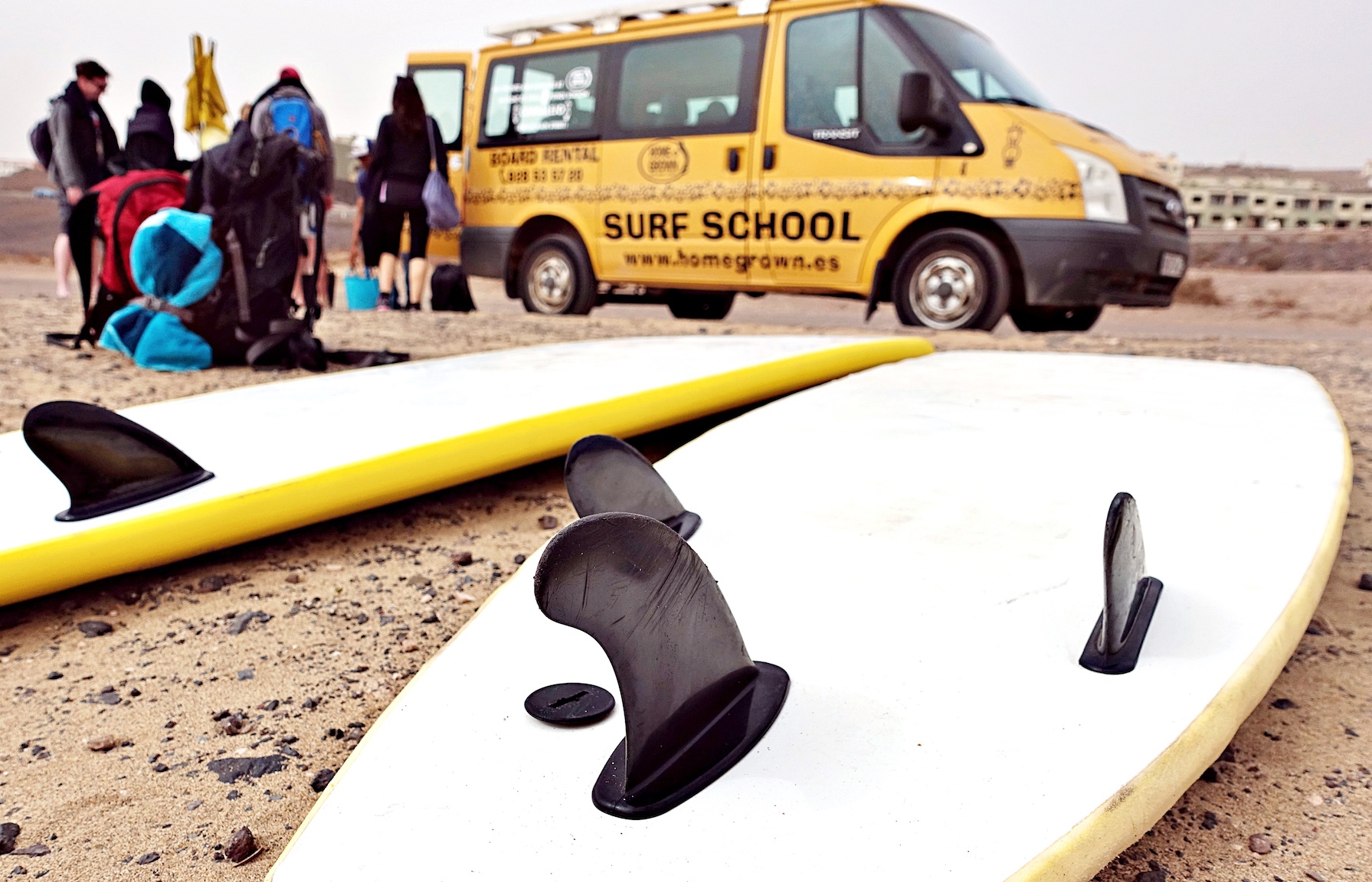 Surfboards on the sand with yellow van in the background