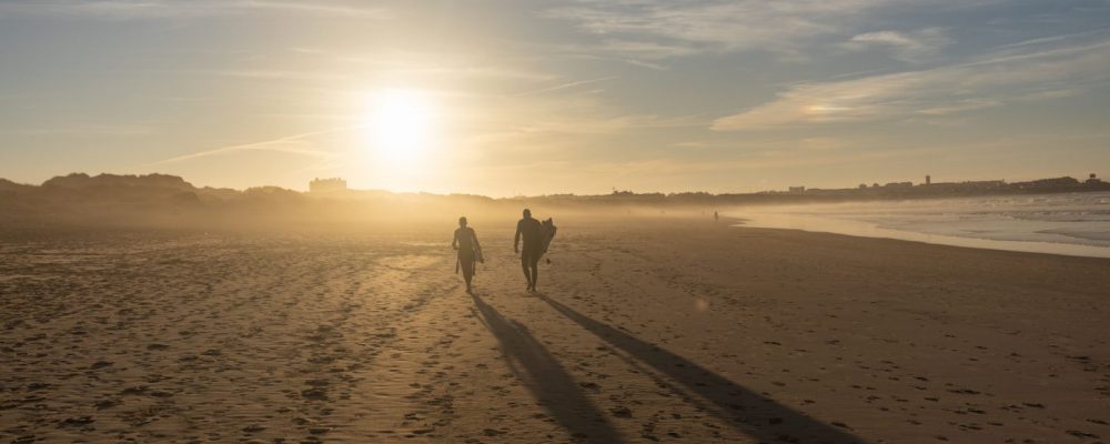 surfers on a beach at sunset - the history of surfing