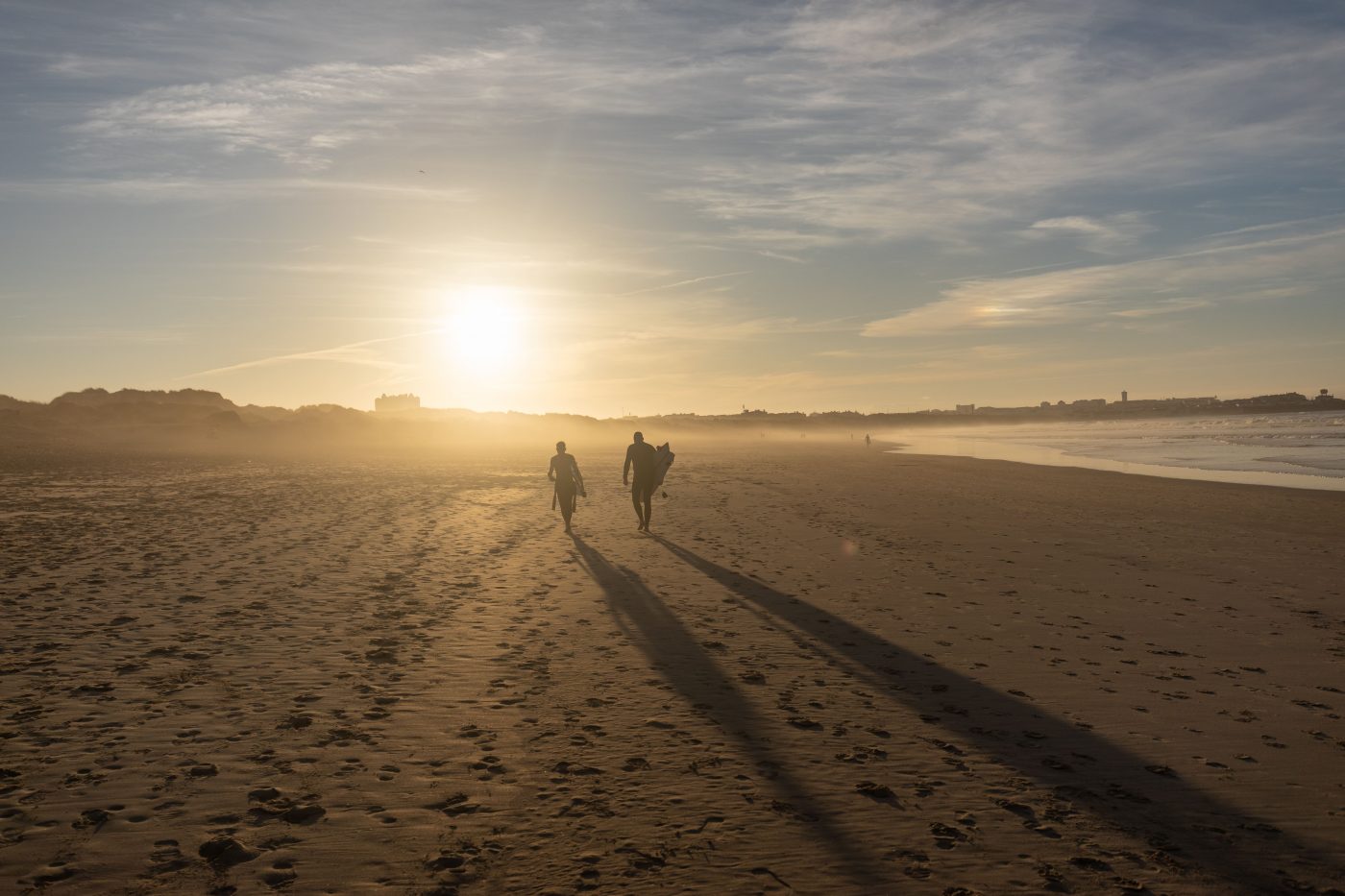 surfers on a beach at sunset - the history of surfing