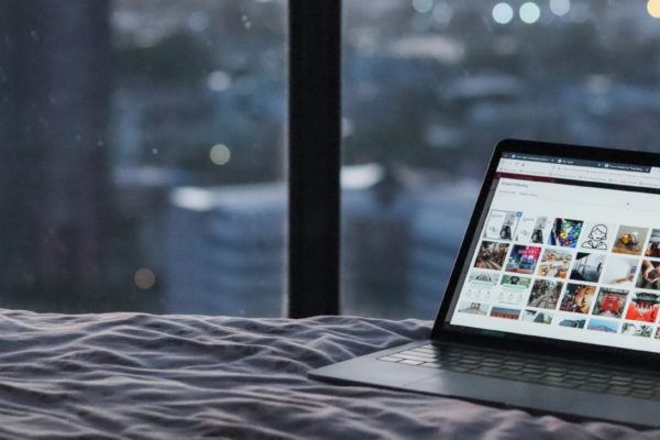 A laptop on a hotel bed with a blurred city view through the window in the background.