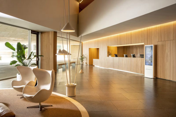 Photo of the reception at Palm Bay at an 45 angle. There's a cream leather chair on a round brown rug with a cream edge on the left. The reception desk on the right with glass doors facing the street in the background.