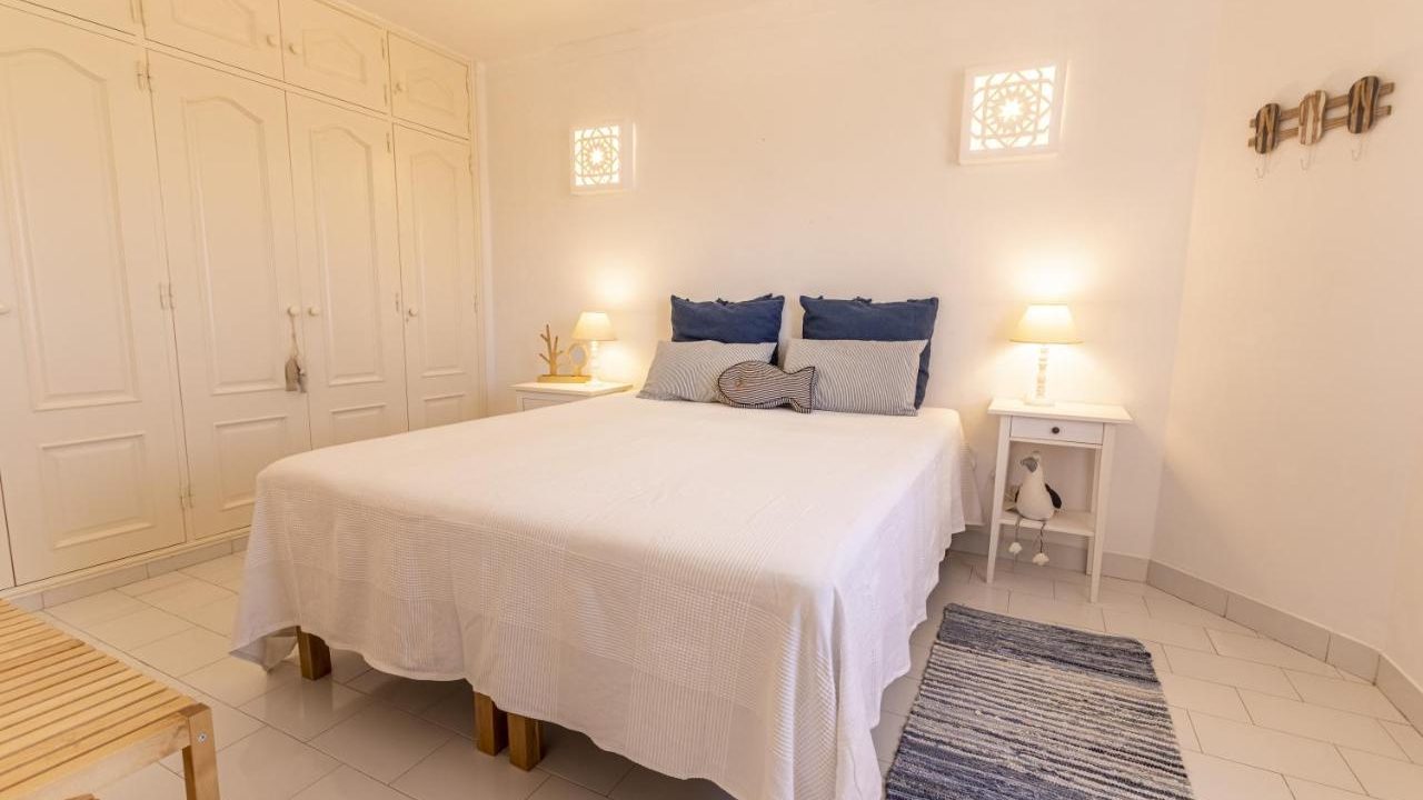 A totally white bedroom at the Azul apartment with two navy and two grey pillows on the bed.