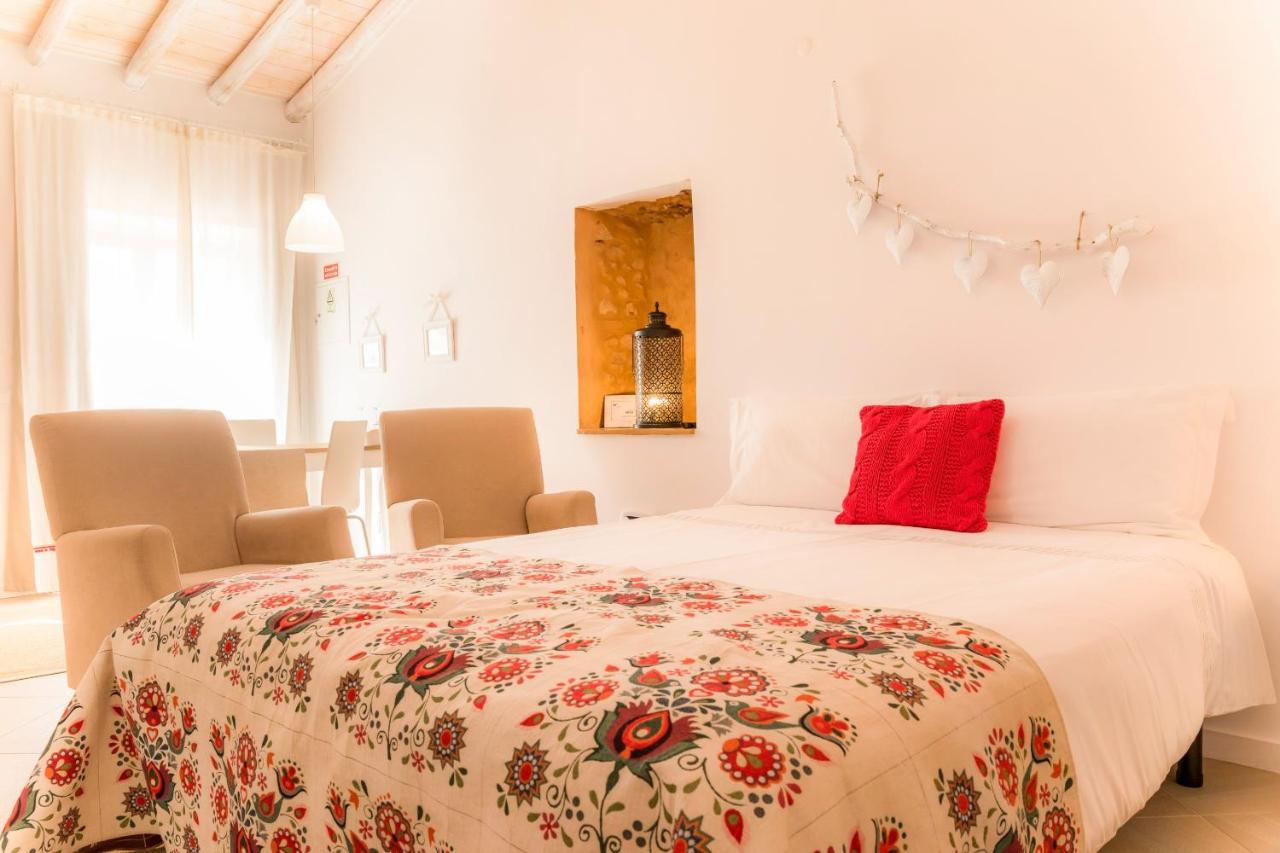 A white room with a double bed with chairs placed facing the bed next to it.